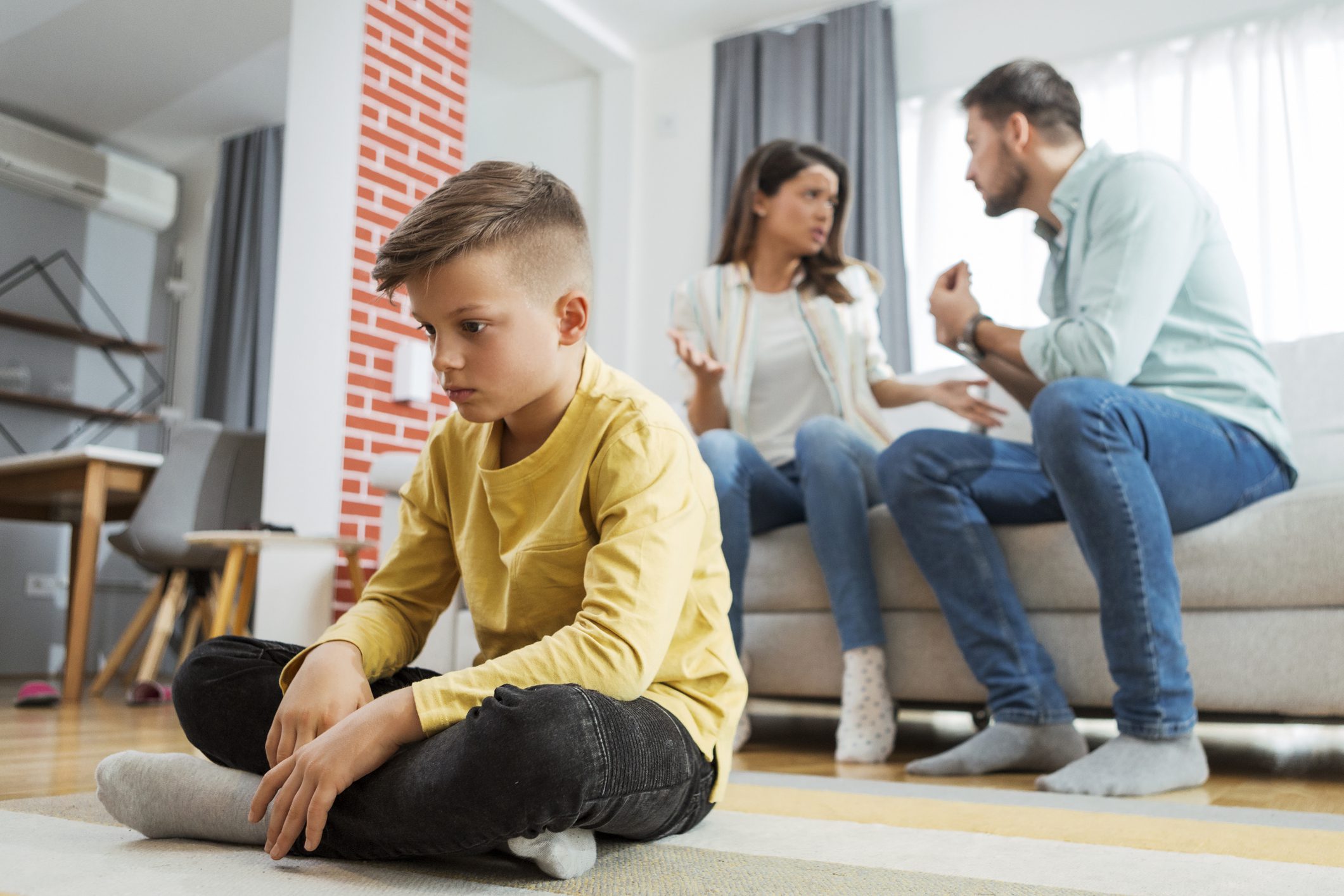 Child sitting while parents argue on sofa.